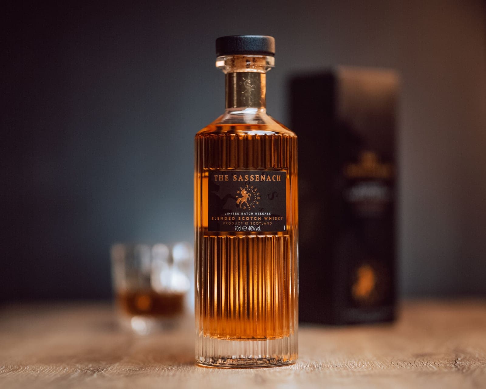 A whiskey bottle beside a wrapped gift box on a wooden table