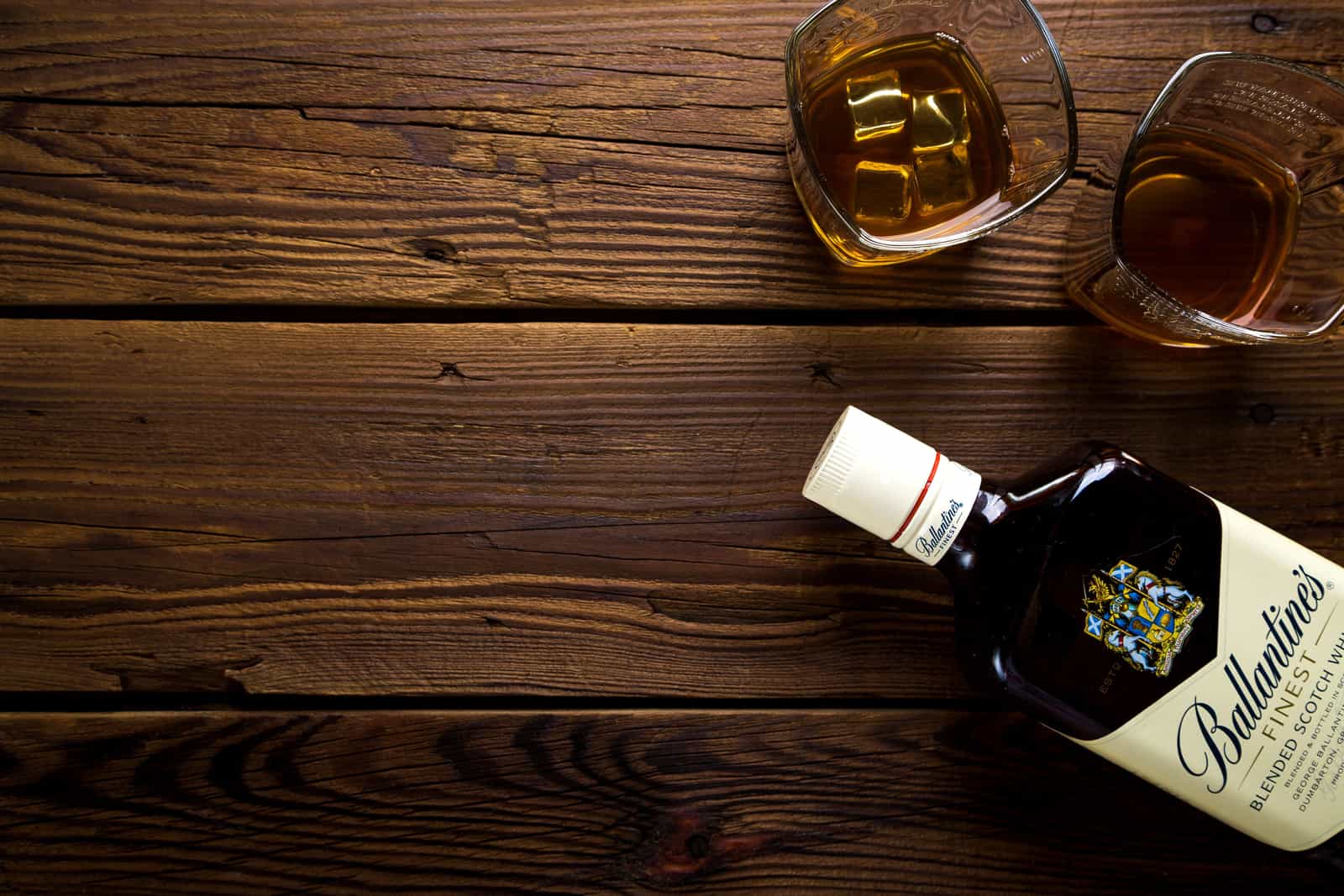 A whiskey glass with ice on a dark wooden surface in warm light